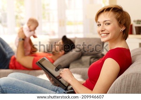 Happy young woman using tablet pc at home, family playing at background.