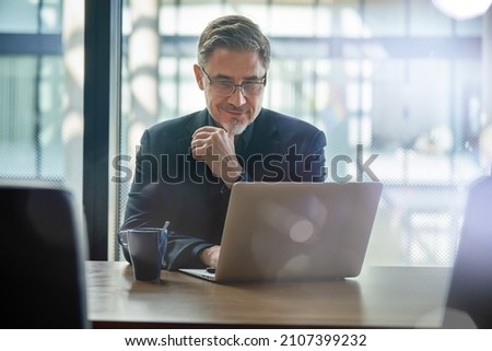 Business portrait - businessman sitting in in office working with laptop computer. Mature age, middle age, mid adult man in 50s with happy confident smile. Copy space. Foto stock © 