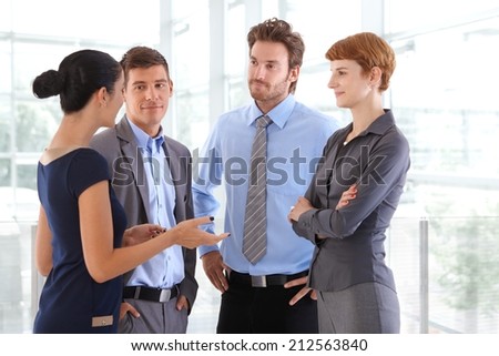 Corporate people chatting at business office lobby. Standing, gesturing, arms crossed, arms on hip, confident, wearing suit, confident.