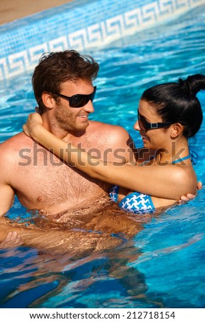 Loving couple enjoying summer holiday in swimming pool, smiling.