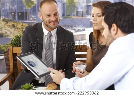 Happy smiling caucasian businessman doing presentation to office workers with tablet computer, outdoor. Suit and tie.