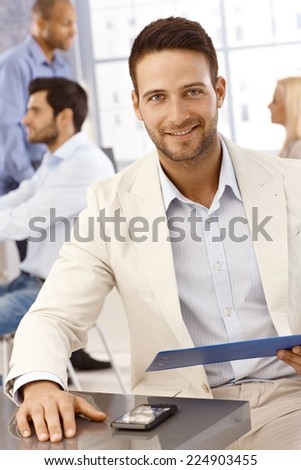 Closeup portrait of happy young handsome businessman, smiling at camera, sitting by table.