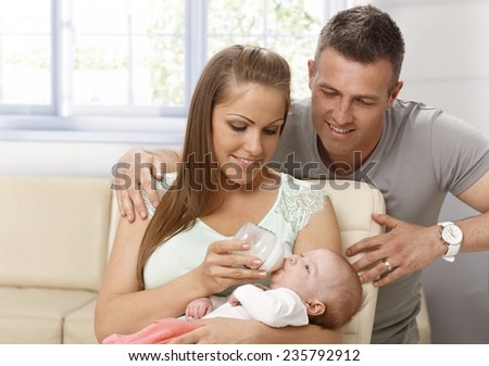 Happy mother feeding and caressing newborn baby, father hugging them.