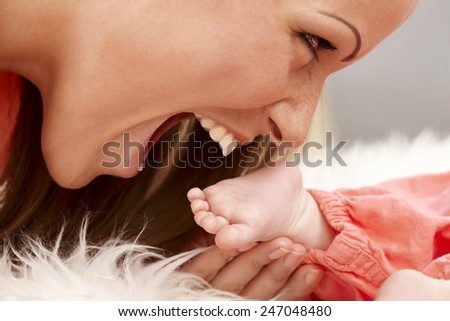 Closeup photo of mother holding and biting tiny bare baby foot. Side view.