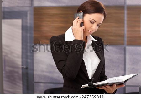 Young businesswoman talking on mobilephone, looking at personal organizer.