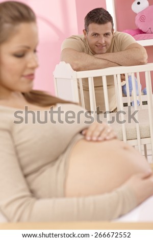 Proud young father looking at pregnant wife, smiling.