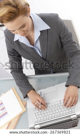 Above view of businesswoman working on laptop, sitting at desk in office, typing on keyboard.