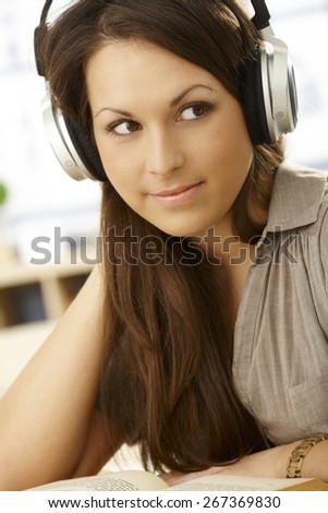 Closeup portrait of attractive young woman with headphones and book, smiling, looking away.