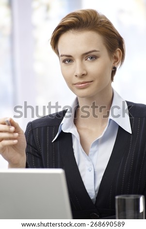 Portrait of attractive young businesswoman working with computer, looking at camera.