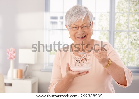 Happy old woman eating breakfast cereal, smiling, looking at camera.