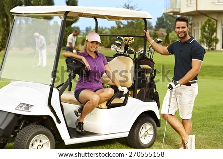 Happy golfers sitting in golf cart, smiling, looking at camera.