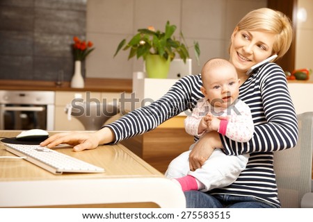 Businesswoman working from home, holding baby girl on lap.