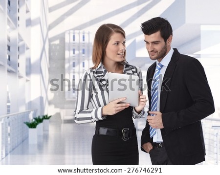 Formal clothed business partners holding tablet discussing at office, smiling.