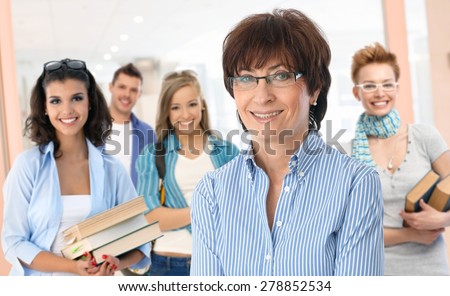 Portrait of happy senior female teacher with group of students in background.