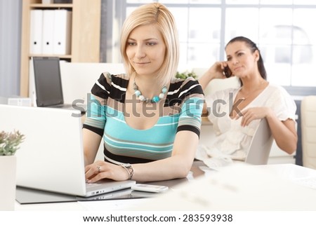 Happy casual caucasian blonde businesswoman working with laptop computer at office, smiling.