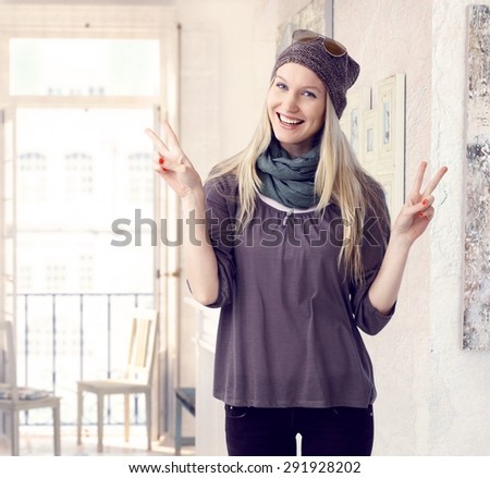 Successful happy caucasian casual blonde creative artist woman at retro home. Standing, smiling, looking at camera, giving the victory sign.