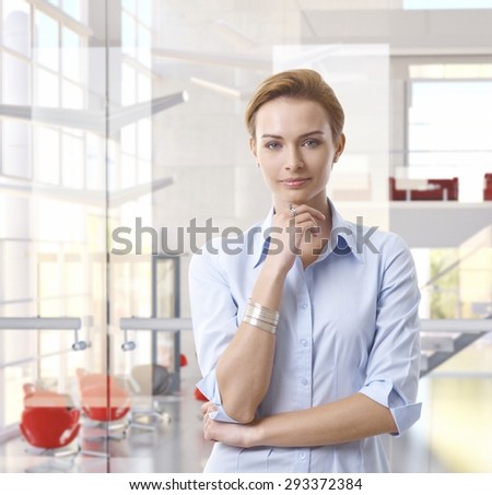 Casual attractive caucasian businesswoman standing at classy bright business office, looking at camera, hand under chin, copyspace.