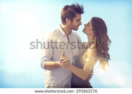 Happy loving couple embracing and kissing outdoors at summertime under blue sky.