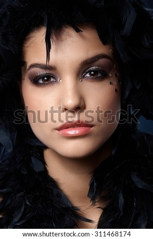 Closeup facial portrait of extravagant beauty with glittering makeup and black feather boa.