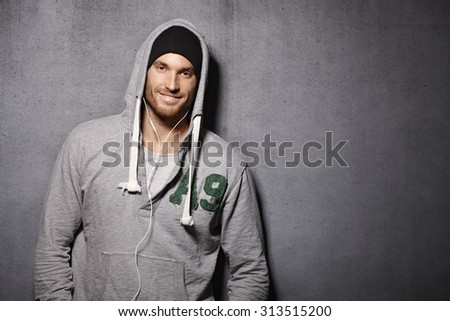 Urban style young man smiling happy, leaning against grey wall, wearing ...