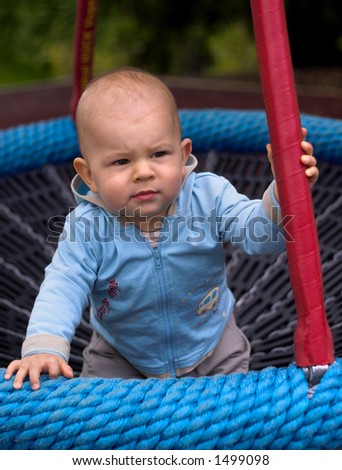 A baby is playing on a playground, he is sitting in a baby-swing.