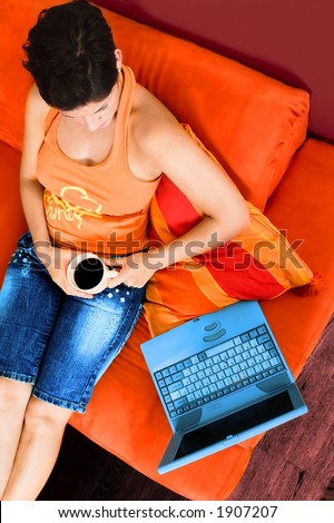 Young women is lying on the couch at home and using a notebook computer.