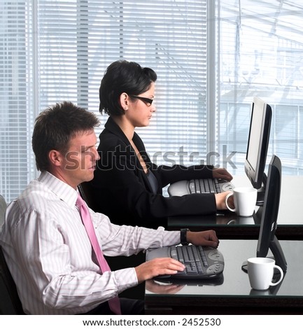 Young, good looking and well-dressed office workers are working on similar desktop computers in a modern office.