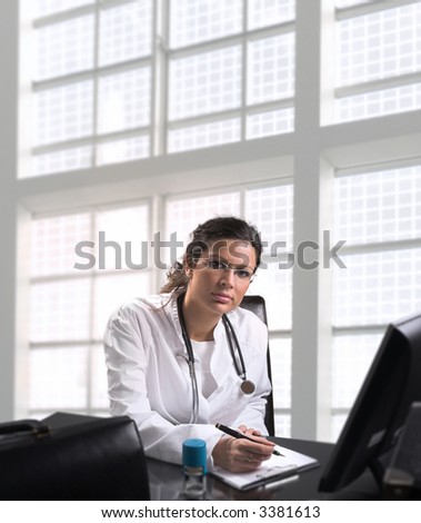Young female doctor sits by desk in  doctor\'s office. Daylight, indoor.
