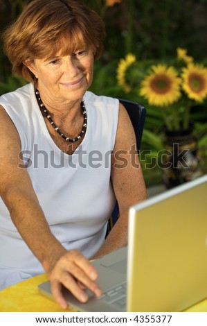 Modern senior woman sitting in the garden at home and using a laptop computer. Summer, outdoor.