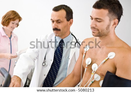 Medical team performing an EKG test on  young male patient. Real people, real location, not a staged photo with models. Focus is placed on the doctor.
