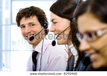 Customer service team working in headsets. Focus placed on smiling man in back.