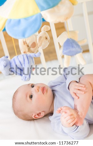 Little baby boy (4 months old) lying on crib and looking up to hanging toy, smiling. Toys are officially property released.