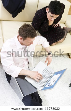 Businessman sitting on floor and teamworking on laptop computer with businesswoman. They look workaholic. High-angle view.