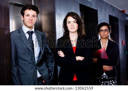 Portrait of successful happy business team posing at office lobby in front of elevator. Dark background.