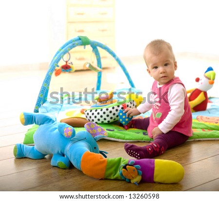Baby Girl (9 months old) sitting on floor and playing with toys at home in living room. Toys are property released.