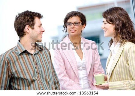 Happy young casual business people standing side by side in fornt of office window, talking and smiling.
