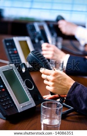 Close-up of hands holding landline phone recievers at customer service office.