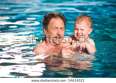 Grandfather and grandson swimming together in the pool. Outdoor, summer.