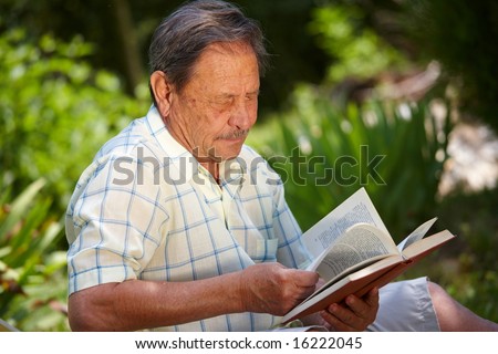 Healthy looking old man is his late 70s sitting in garden at home and reading book.
