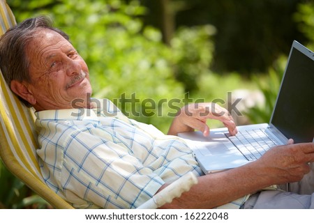 Happy senior man is his elderly 70s sitting outdoor in garden at home and using laptop computer to browse internet, smiling.