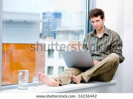 Businessman sitting in office window and working on laptop computer, wireless technology.