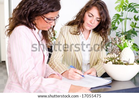 Casual businesswomen working together in team at office reception, looking at documents, talking.