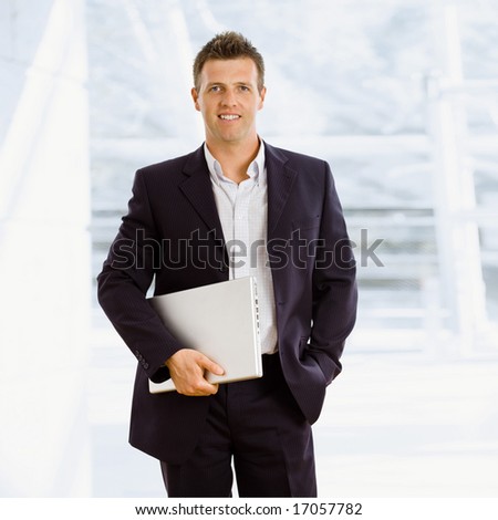 Happy businessman holding laptop computer indoor smiling
