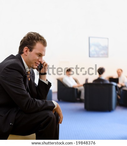 Businessman calling on mobile phone at office lobby, smiling.