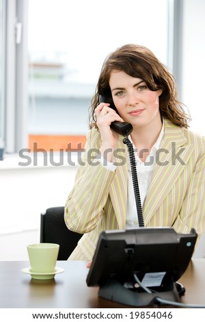 Young female telephone worker holding landline phone at office, smiling.