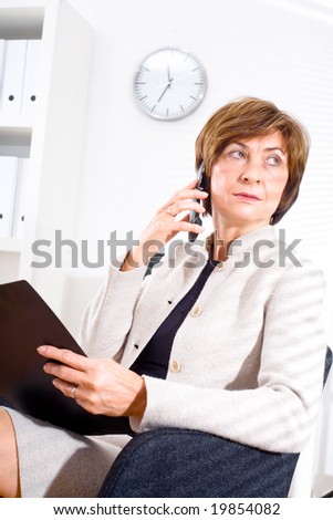 Senior businesswoman looking through window while calling on phone and working at office.