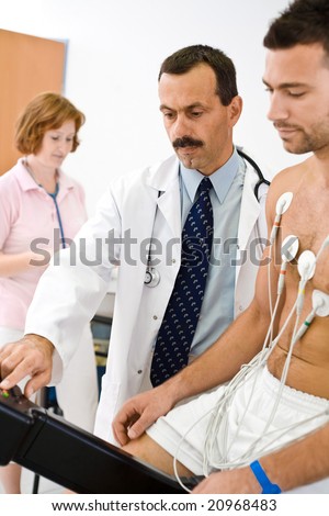 Medical team performing an EKG test on  young male patient. Real people, real locacion, not a staged photo with models. Focus is placed on the  doctor.