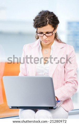 Young attractive businesswoman working on laptop computer in fron front of office window.