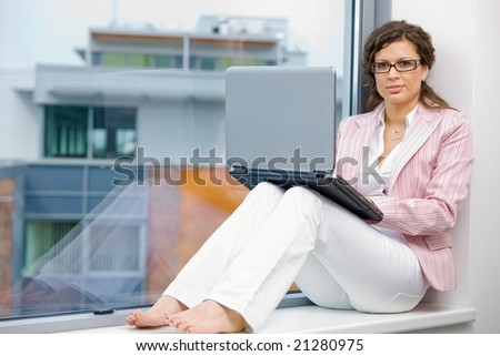 Young creative businesswoman sitting at office window and working on laptop computer.