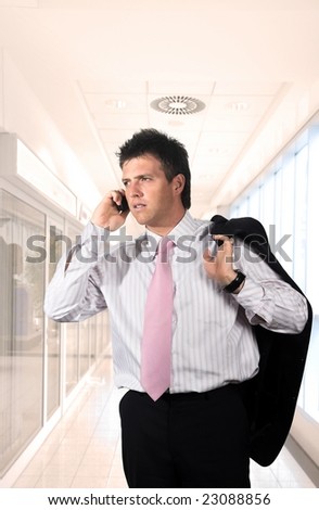 Young and handsome businessman walks on a modern office corridor and talkes on mobile phone.